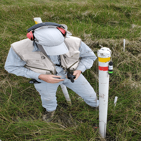 Person holds small instument piece while standing next to a white pole in the grassland