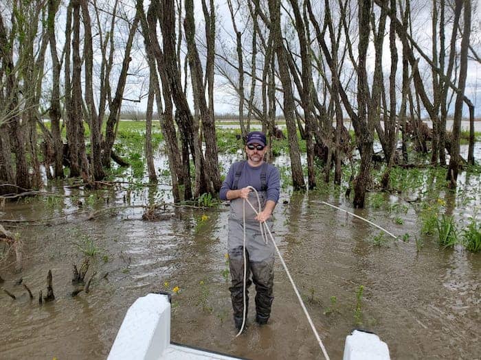 Mike holds a rope while standing ankle-deep in the marsh water