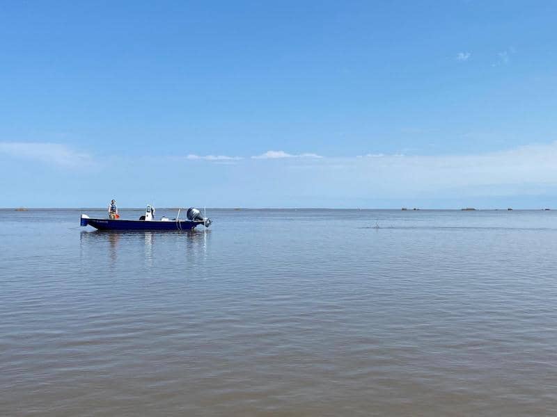 A small blue boat floats in the water at a distance, a single person sitting inside