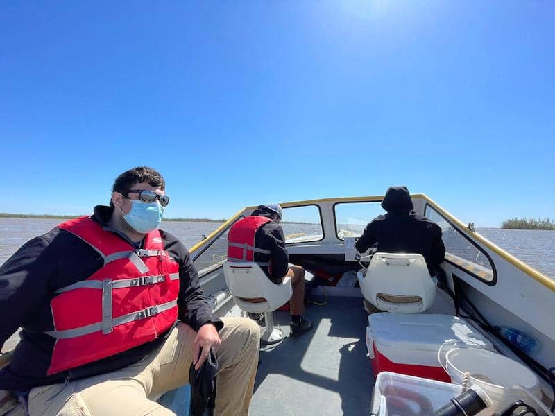 Three people on a boat with masks and life jackets on, one looking out