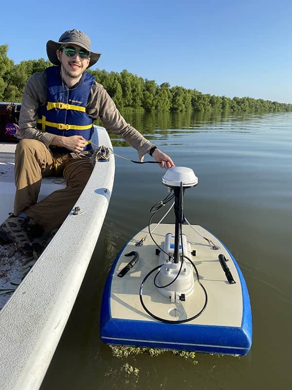 Michael sits in a boat holding a cable connected to the ADCP instrument floating in the water next to him