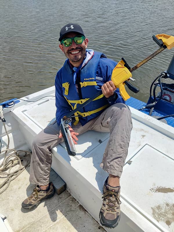 Talib smiles while holding an instrument in a boat