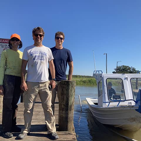 Three team members stand smiling on the boat dock