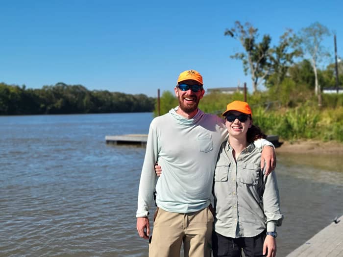 John and Wayana stand smiling with a delta water channel in the background