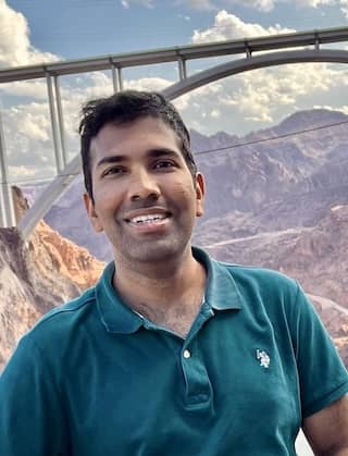 Bhuvan smiles with a bridge and dry mountains in the background