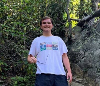 Brandon Wolff stands smiling in front of a forested area