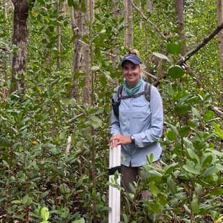 Emily stands in a forest, holding an measuring instrument