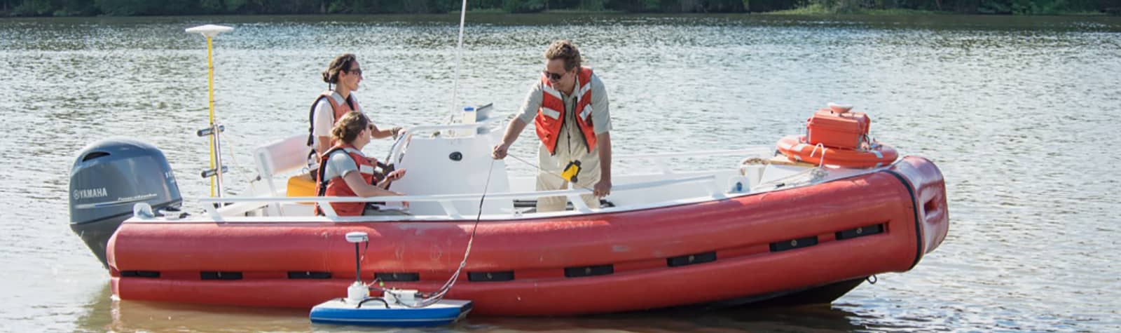 Two women and a man operate field instruments in an orange airboat