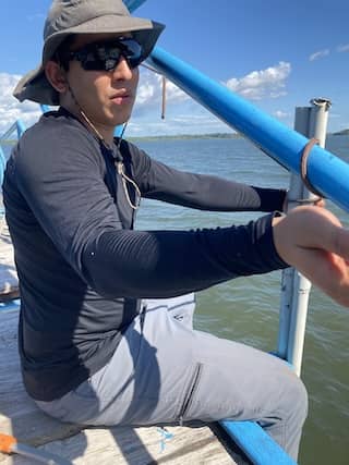 Ivan holds an instrument while sitting on a boat with a neutral expression