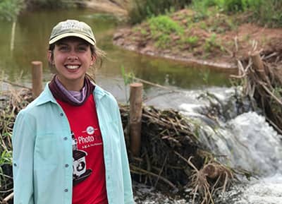 Julianne stands smiling in front of a tiny waterfall