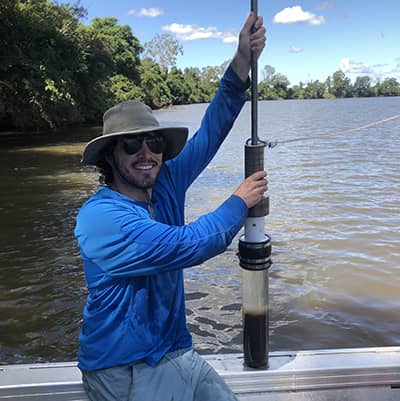 John smiles at the camera while holding an instrument upright in a boat