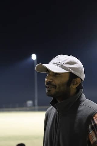 Pradipta wearing a hat and looking into the distance with a single light and field behind him on a dark night