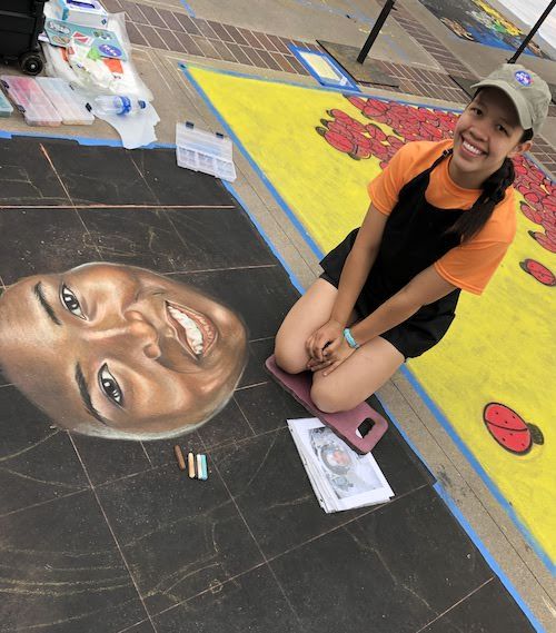 Sarah Flores kneels next to her work-in-progress street painting of Mae Jemison's face